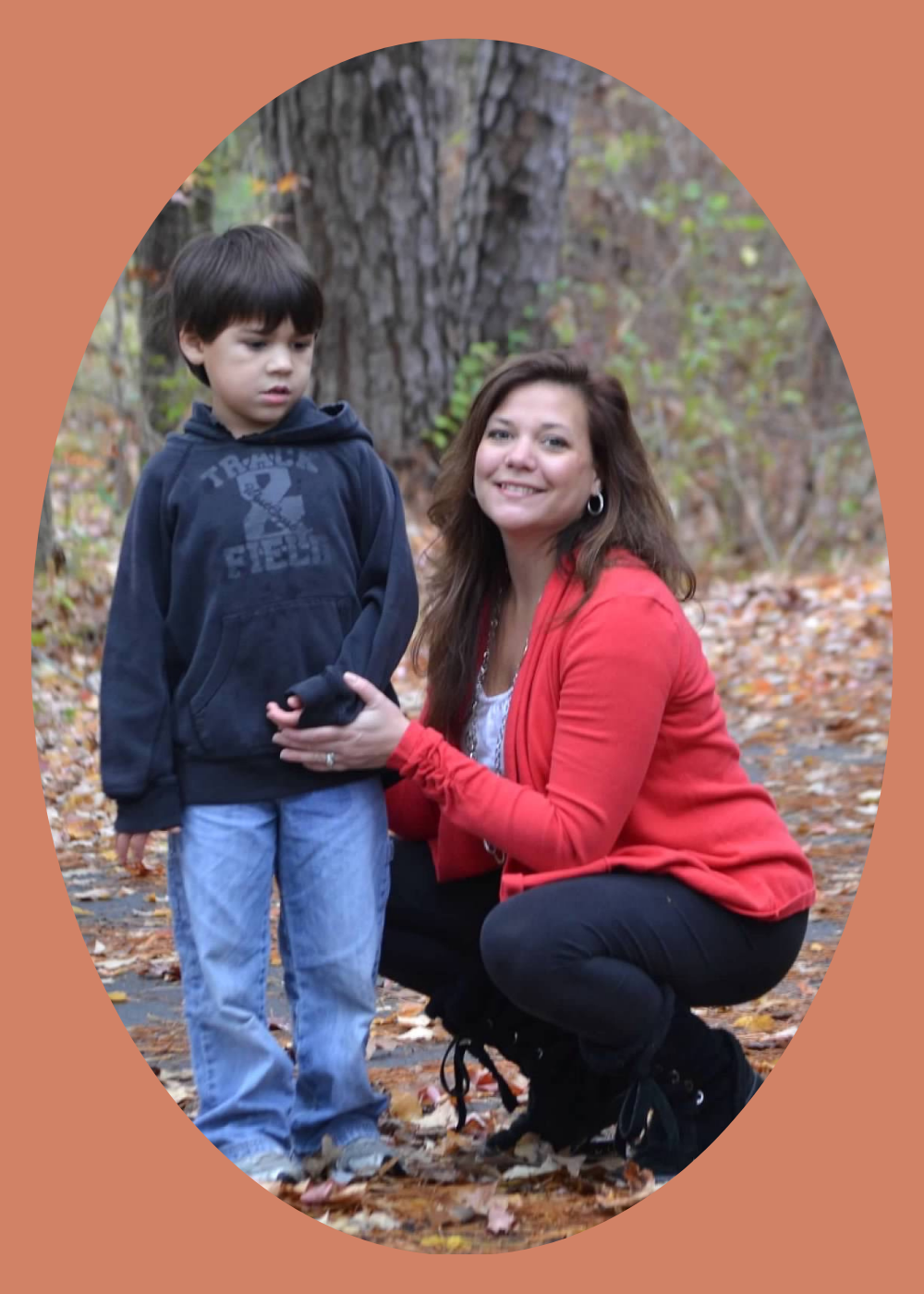 Christy kneels to the right of her autistic son. They are outside during autumn, on a paved path. Fallen leaves surround them.