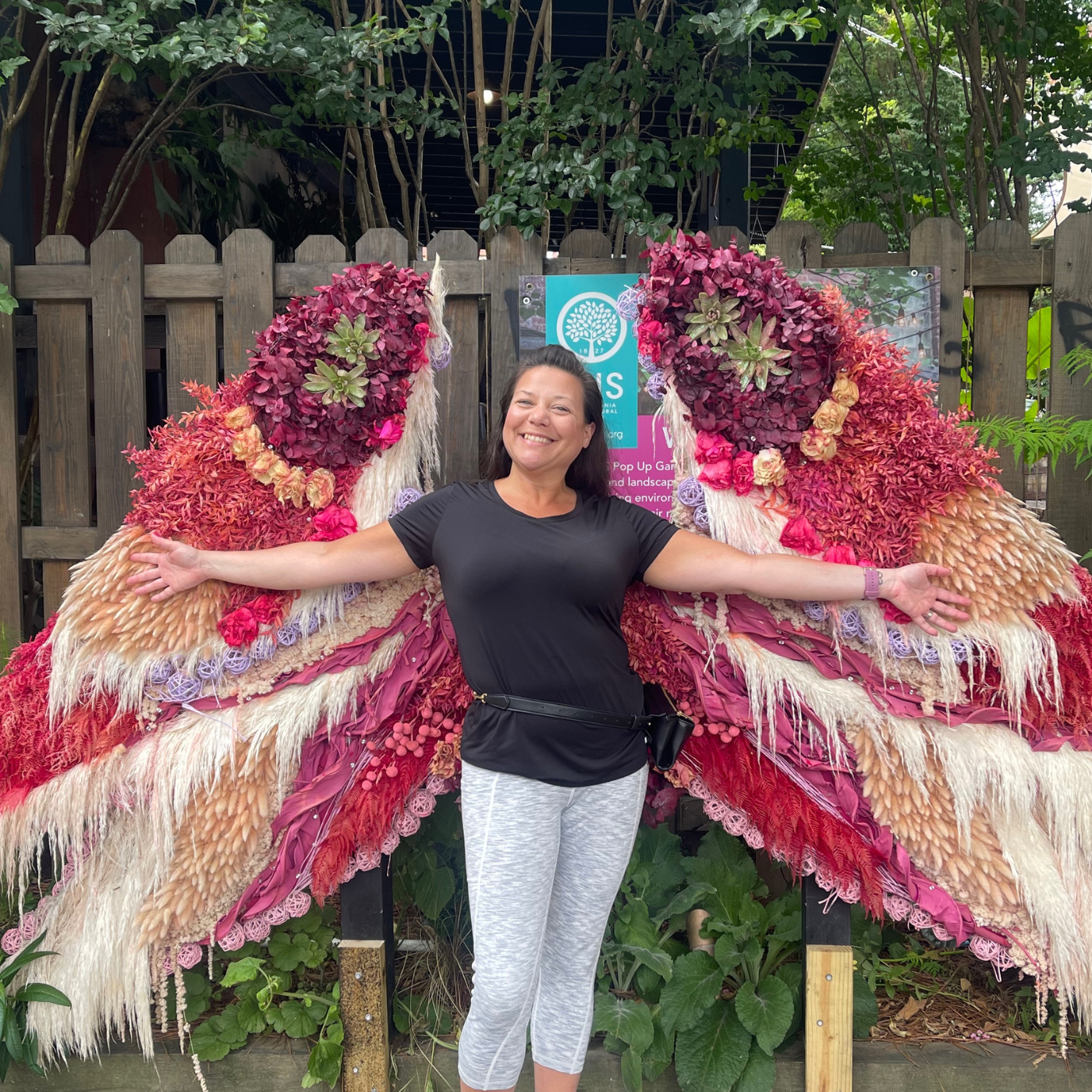 Christy stands in front of large butterfly wings made of flowers.