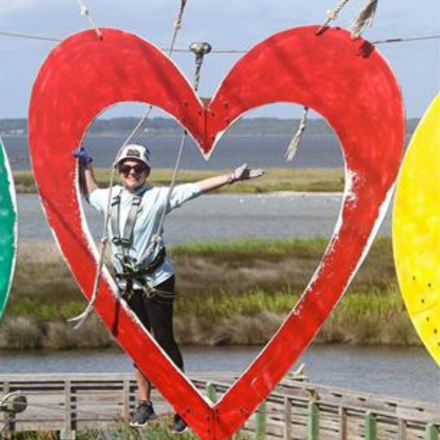 Christy hangs from a zip line and is centered in a large red heart, hanging high from the sky.