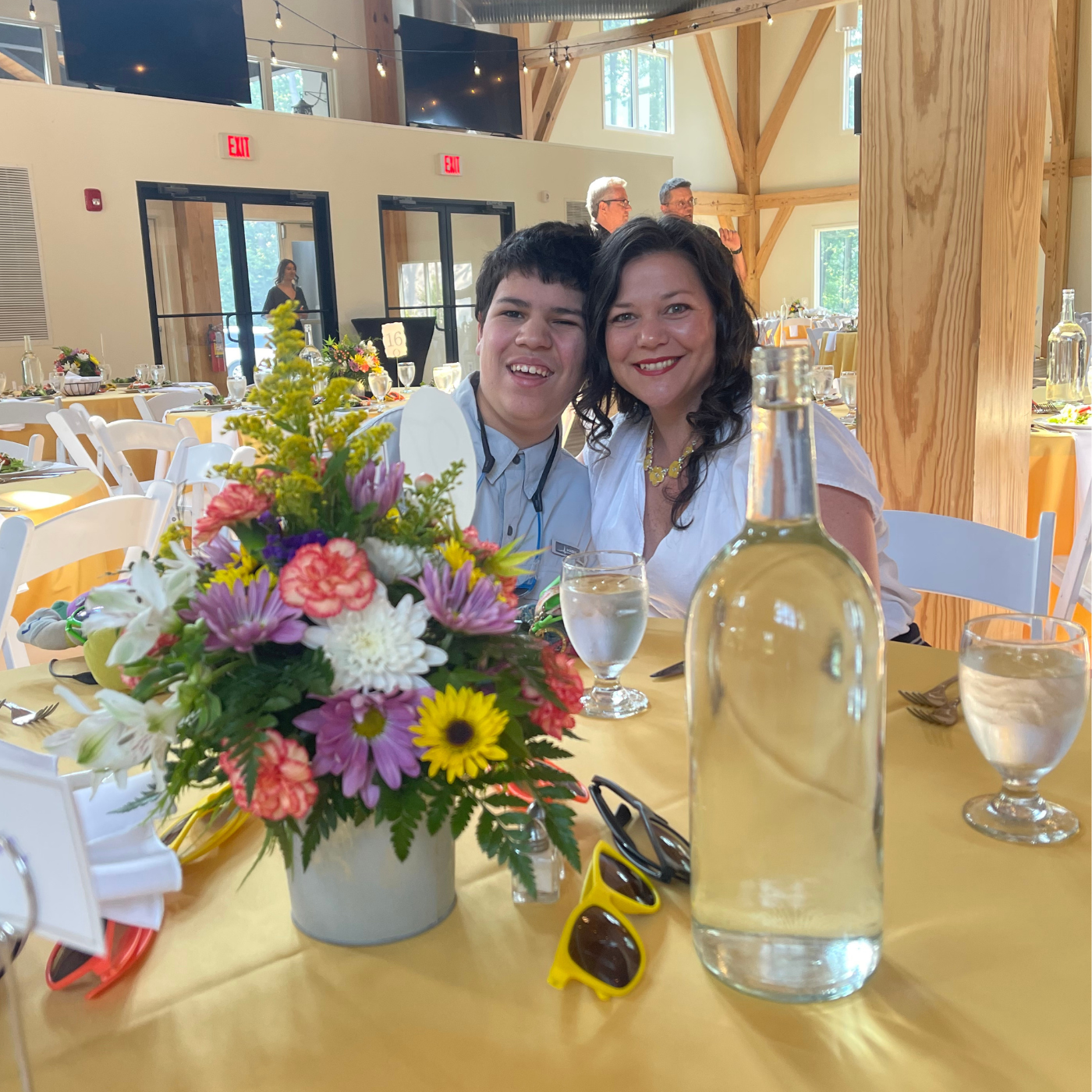 Christy and her son, "C" sit at a round table with a yellow table cloth and bouquet of bright flowers. They attended the Sunshine Ball together, a dance for people with developmental disabilities.